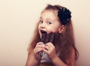 Happy smiling kid girl biting tasty chocolate with empty copy space. Vintage portrait